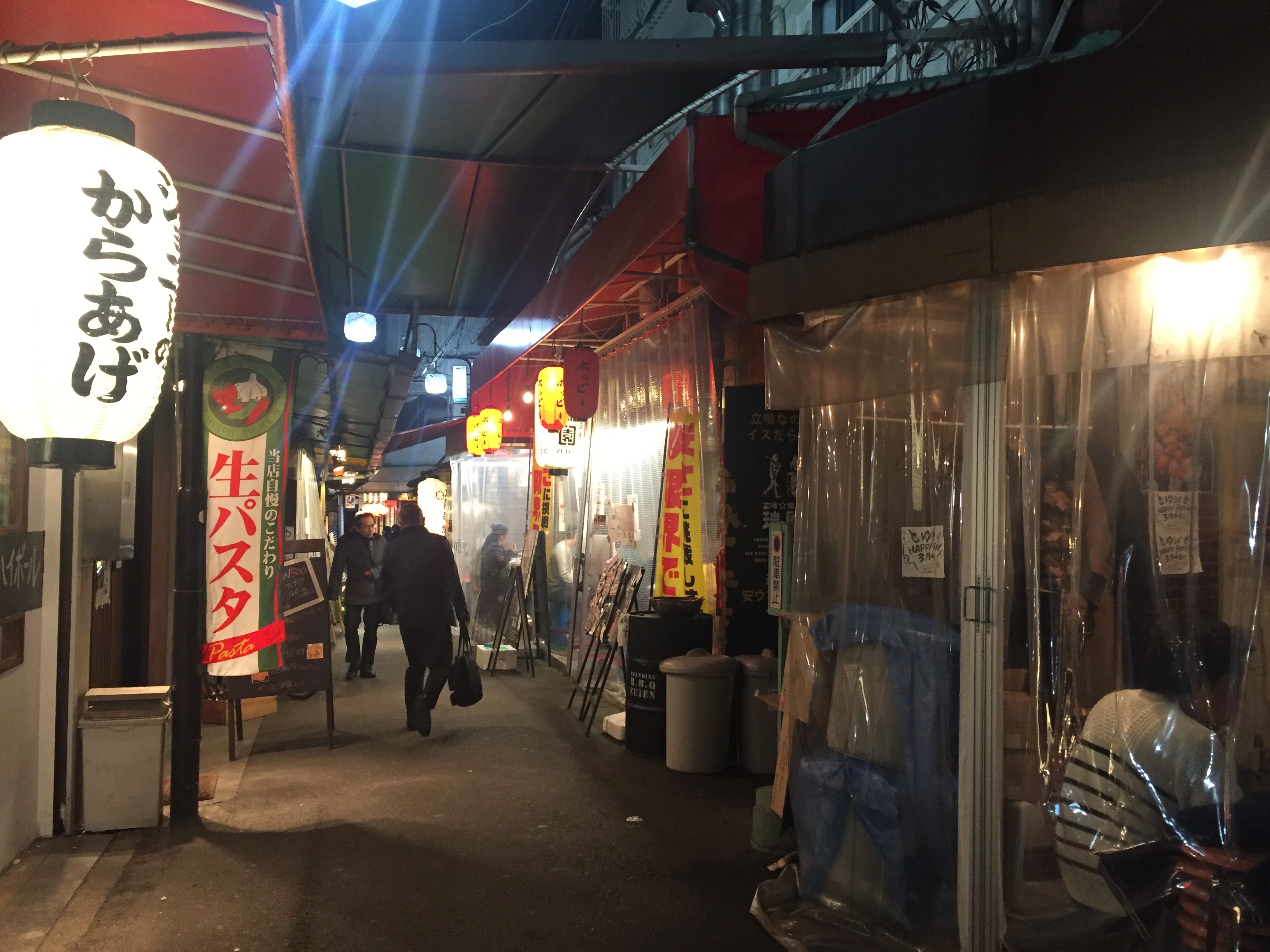 A narrow Japanese alley at night with small restaurants, lanterns, and pedestrians, photographed during my 2018 trip to Japan.